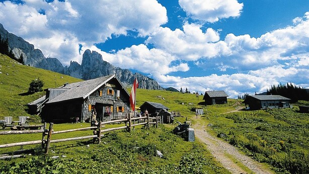Un pittoresco villaggio montano in campagna con case in legno tradizionali, cielo sereno e montagne sullo sfondo.