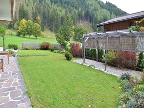 Un jardin bien entretenu, agrémenté d’un chemin de pierre, d’une pergola en bois et offrant une vue sur une colline boisée.