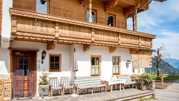 Ein traditionelles Holzchalet mit Balkon, Steintreppe und Sitzgelegenheit im Freien.