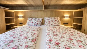 Un lit double avec une literie à motifs floraux, dans une pièce aux murs en bois et dotée d’étagères intégrées.