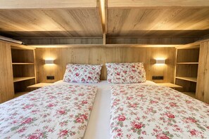 Ein Doppelbett mit floralem Bettzeug in einem Zimmer mit Holzwänden und eingebauten Regalen.
