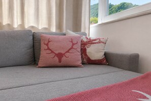 Un sofá gris con dos almohadones decorativos con estampado de ciervo rojo.