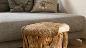 Un canapé gris agrémenté de coussins décoratifs et un tabouret en bois dont l’assise est recouverte d’un matériau qui ressemble à de la fourrure.