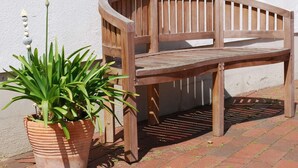 Un banc en bois doté d’un dossier à lattes et d’une assise plate, placé contre un mur blanc.