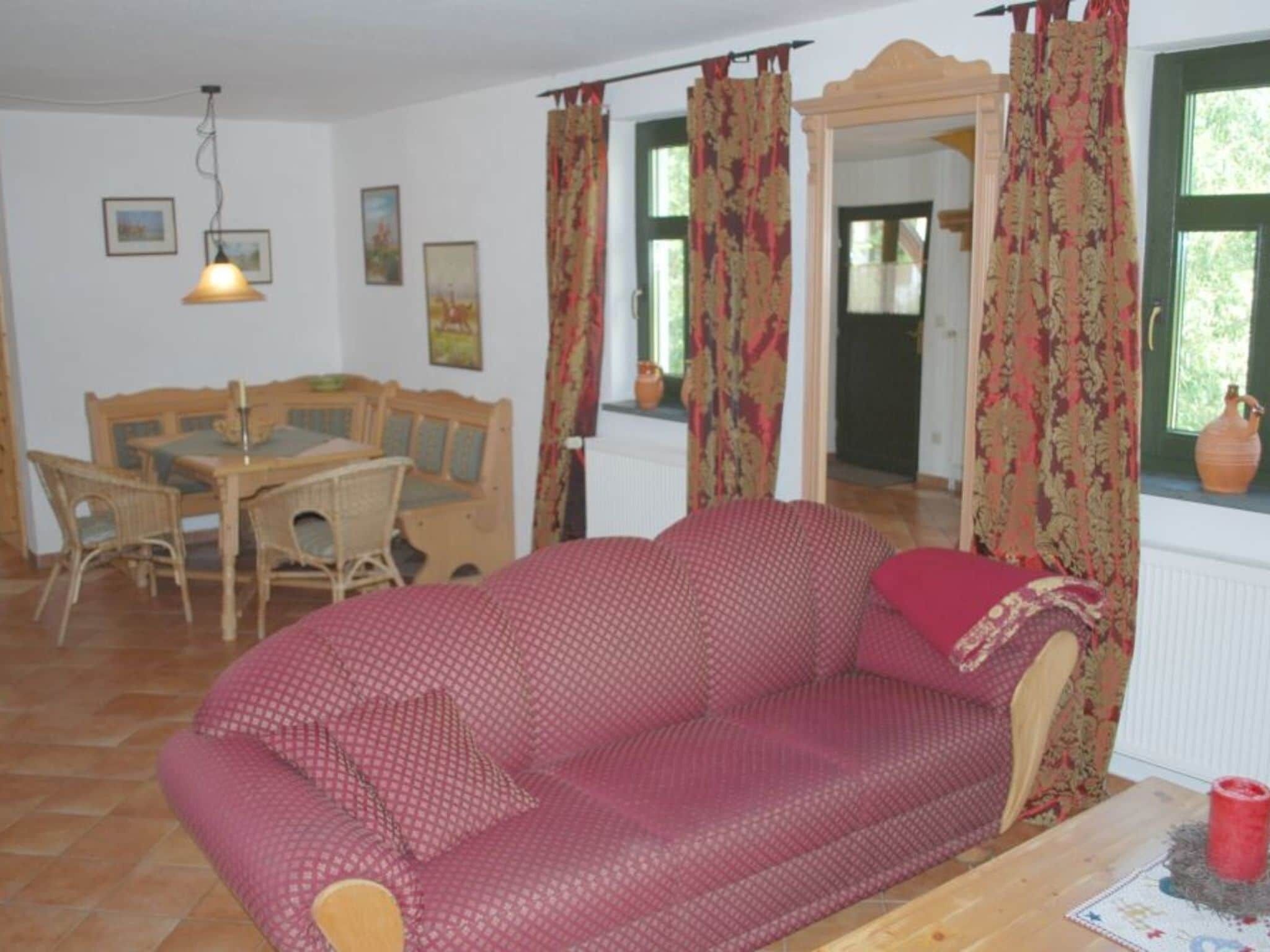 A cozy living room with a patterned sofa, a wooden dining table with chairs, and a window with curtains.