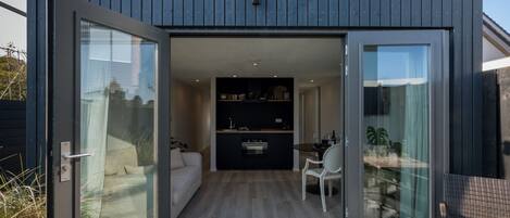 A modern, compact living space with a glass door entrance, a kitchenette, a dining area, and a seating area with a view.