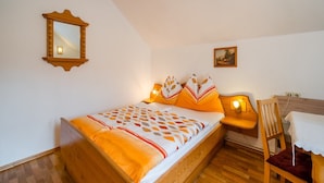 A bedroom with a wooden bed, a nightstand with a lamp, a chair, and a small table with a white tablecloth. - Holiday apartment in Tröpolach (Tröpolach)