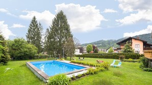 A backyard with a swimming pool, green lawn, and a house with a balcony. - Holiday apartment in Tröpolach (Tröpolach)