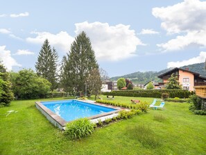 Ein Swimmingpool, umgeben von einer gepflegten Rasenfläche, mit einigen Liegestühlen und einem Pavillon.