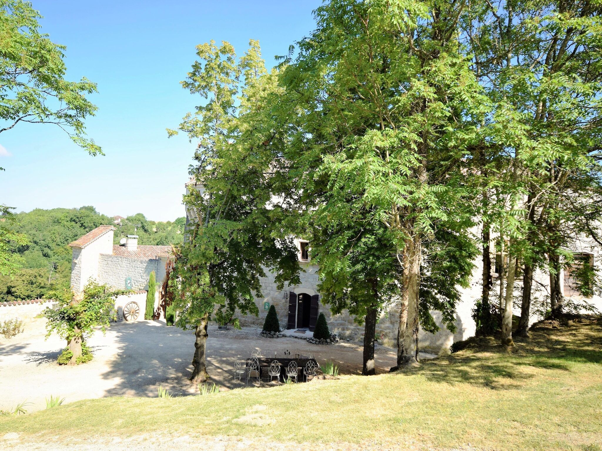 Un bâtiment rustique en pierre, doté d’une façade blanche, entouré d’une végétation luxuriante et d’arbres.