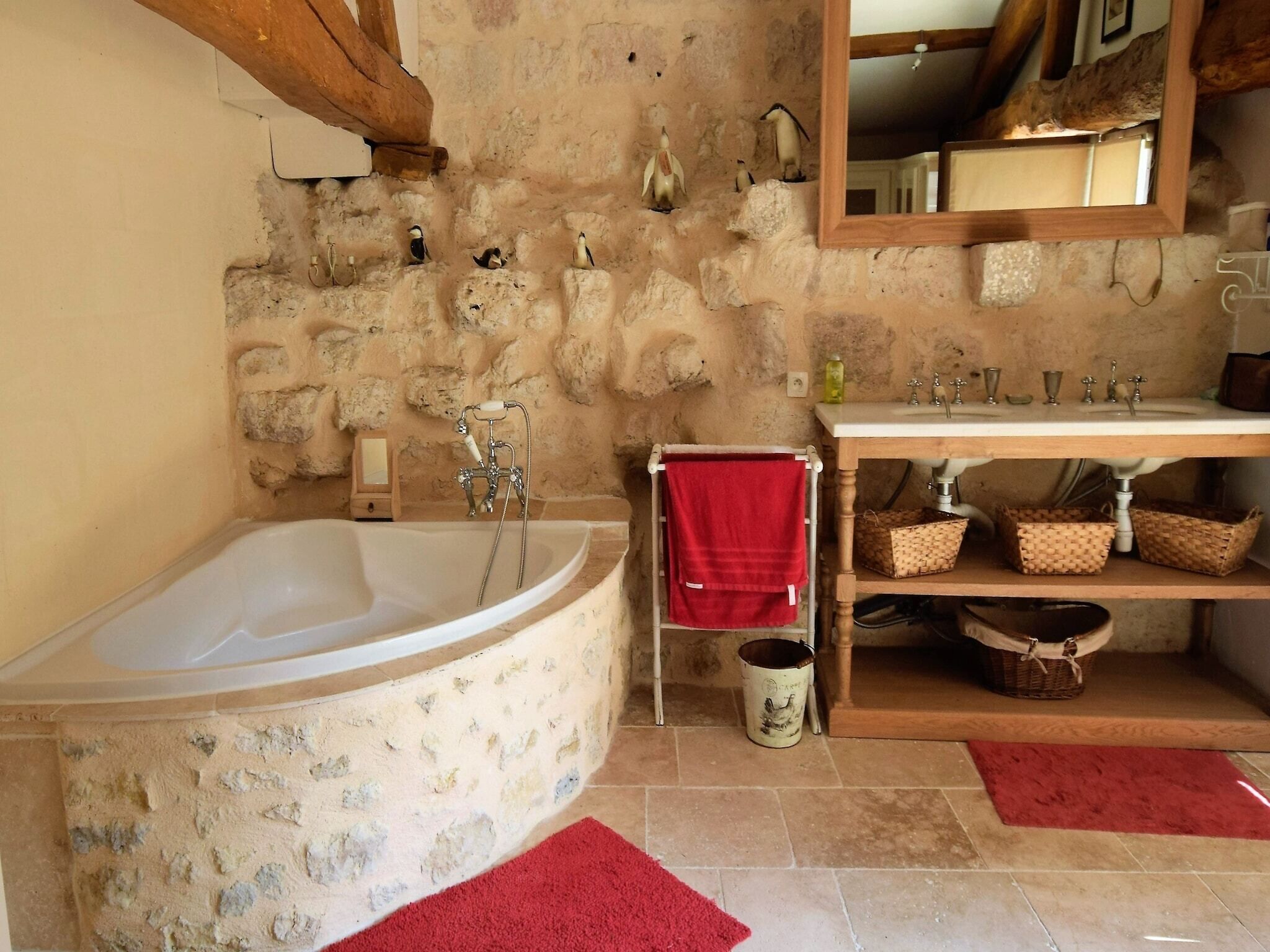 Une salle de bain avec un mur en pierre, un meuble-lavabo en bois, une serviette rouge et une baignoire.