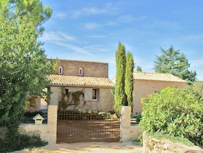 A rustic stone building with a tiled roof, a gated entrance, and surrounding greenery.