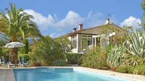 A swimming pool with lounge chairs and a house in the background.