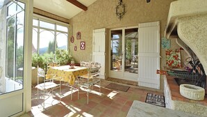 A sunlit dining area with a table and chairs, a view of the outdoors, and a stone fireplace.