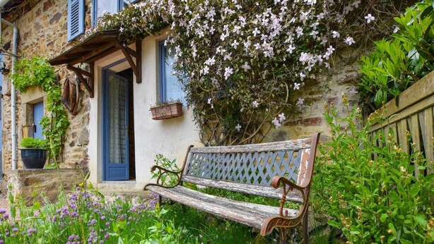 A rustic stone building with a wooden bench in front, surrounded by lush greenery and purple flowers. - Peaceful Getaway in Teilhet (Teilhet)