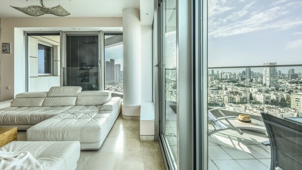 Una sala moderna con un amplio sofá modular, un comedor con mesa y sillas, y vistas a la ciudad a través de grandes ventanales.