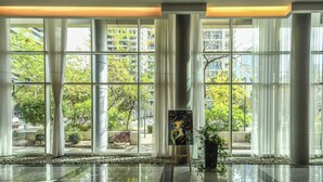 Un vestíbulo amplio con grandes ventanales, una columna central y una planta en maceta.