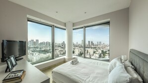 Una habitación de hotel moderna con una cama grande, un escritorio con televisor y vistas a la ciudad a través de amplias ventanas.