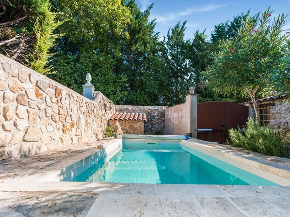 Una piscina con paredes de piedra y techo de baldosas, rodeada de vegetación y una cerca de piedra.