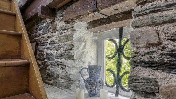 A stone-walled room with a wooden staircase, a window with a metal gate, and two white candles on the windowsill. - Cottage in Saint-Clair-sur-l'Elle (Saint-Clair-sur-l'Elle)