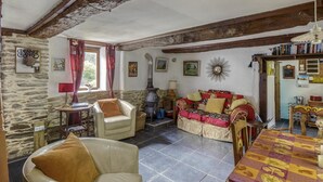 A cozy living room with stone walls, a fireplace, a sofa, and a table with a patterned tablecloth. - Cottage in Saint-Clair-sur-l'Elle (Saint-Clair-sur-l'Elle)