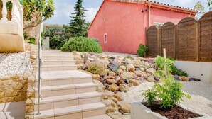 A stone staircase leading to a red building with a tiled roof, surrounded by a garden with rocks and plants. - Holiday home with private pool near Orange (Lagarde-Paréol)