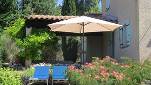 Un patio con dos sillones azules, un paraguas color beige y un muro de piedra con plantas.
