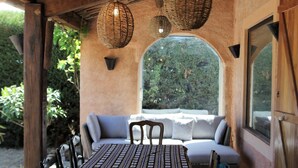 A covered outdoor seating area with a table and chairs, a wicker lamp, and a view of greenery through a window. - Private Pool in Provence (La Motte)