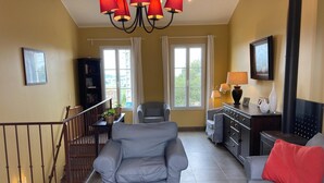 Ein Wohnzimmer mit grauem Sofa, einem Couchtisch mit Pflanze, einer Treppe mit Geländer und einem Kamin.