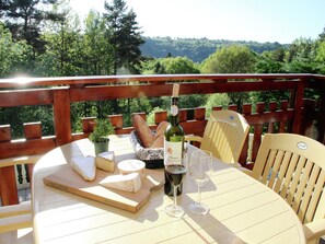 Mesa posta com queijo, pão, vinho e copos em varanda com vista panorâmica.