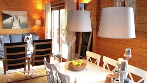 A wooden cabin interior with a dining table, chairs, a bowl of apples, and a painting on the wall. - Poolside Bliss Near Lake (Beaulieu)