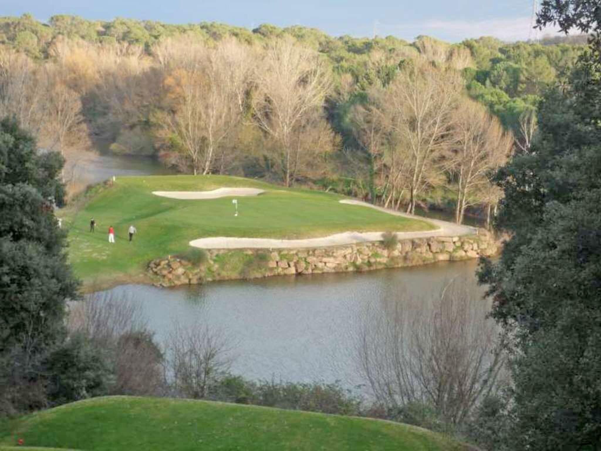 Ein Golfplatz mit einem Wasserschutzgebiet, umgeben von Bäumen und einer Steinmauer.