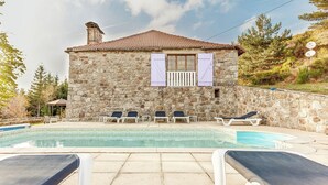 Un edificio de piedra con techo de tejas, piscina y sillas de descanso.