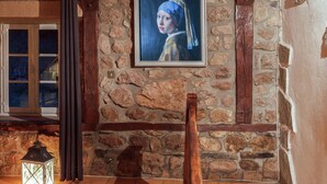 Una habitación con pared de piedra, un cuadro enmarco, una silla de madera y un farol.