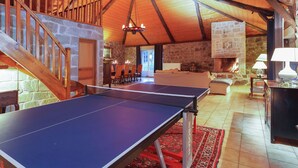 Una habitación amplia con una mesa de ping pong, una chimenea de piedra y una zona de estar acogedora.