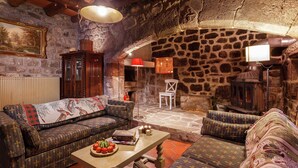 Un salón acogedor con paredes de piedra, un sofá, un sillón y una mesa con un frutero.