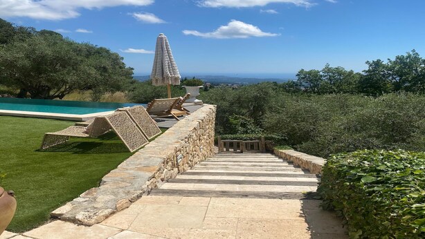 Un escalier en pierre mène à un espace piscine offrant une vue sur une haute tour et une végétation luxuriante.