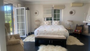 Une chambre avec un grand lit, une chaise, une cheminée et une vue sur l’extérieur, accessible par une porte coulissante.