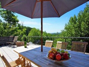 Una terraza exterior con una mesa, sillas y un frutero.