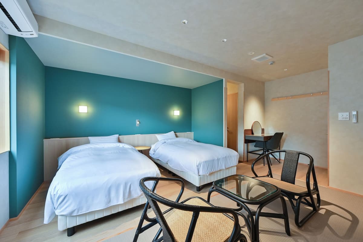 Habitación de hotel con dos camas, una mesita de vidrio y una silla.