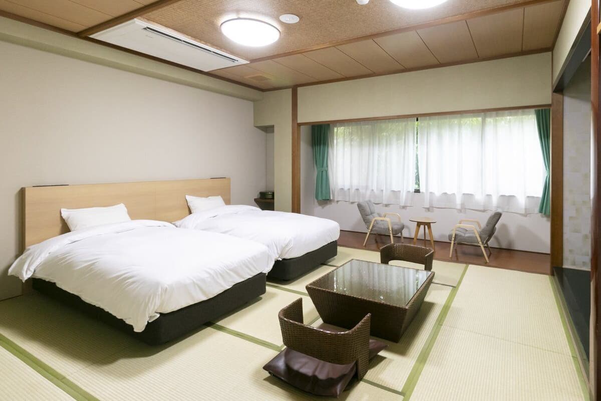 Habitación de hotel con dos camas, una mesita y una zona de estar con sillas.