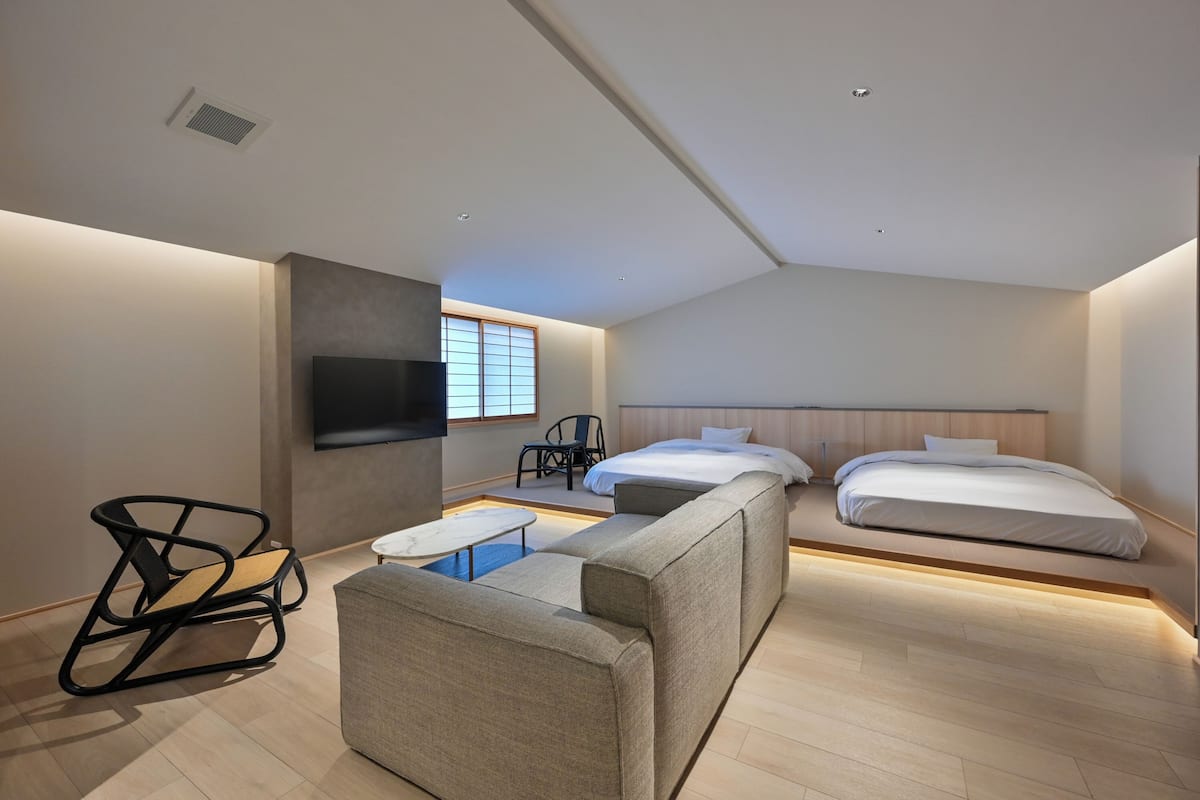 Una habitación de hotel moderna con sofá, una mesita, televisor montado en la pared y dos camas.