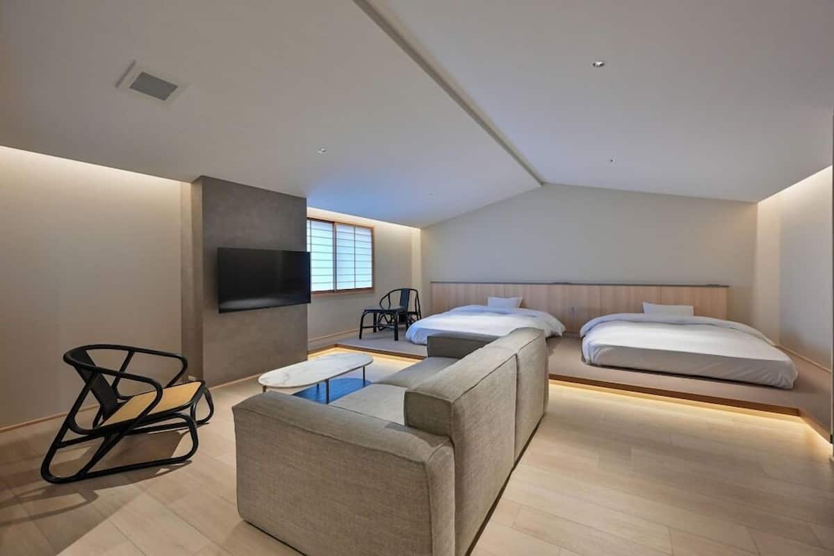 Una habitación de hotel moderna con sofá, dos camas, televisión y ventana.