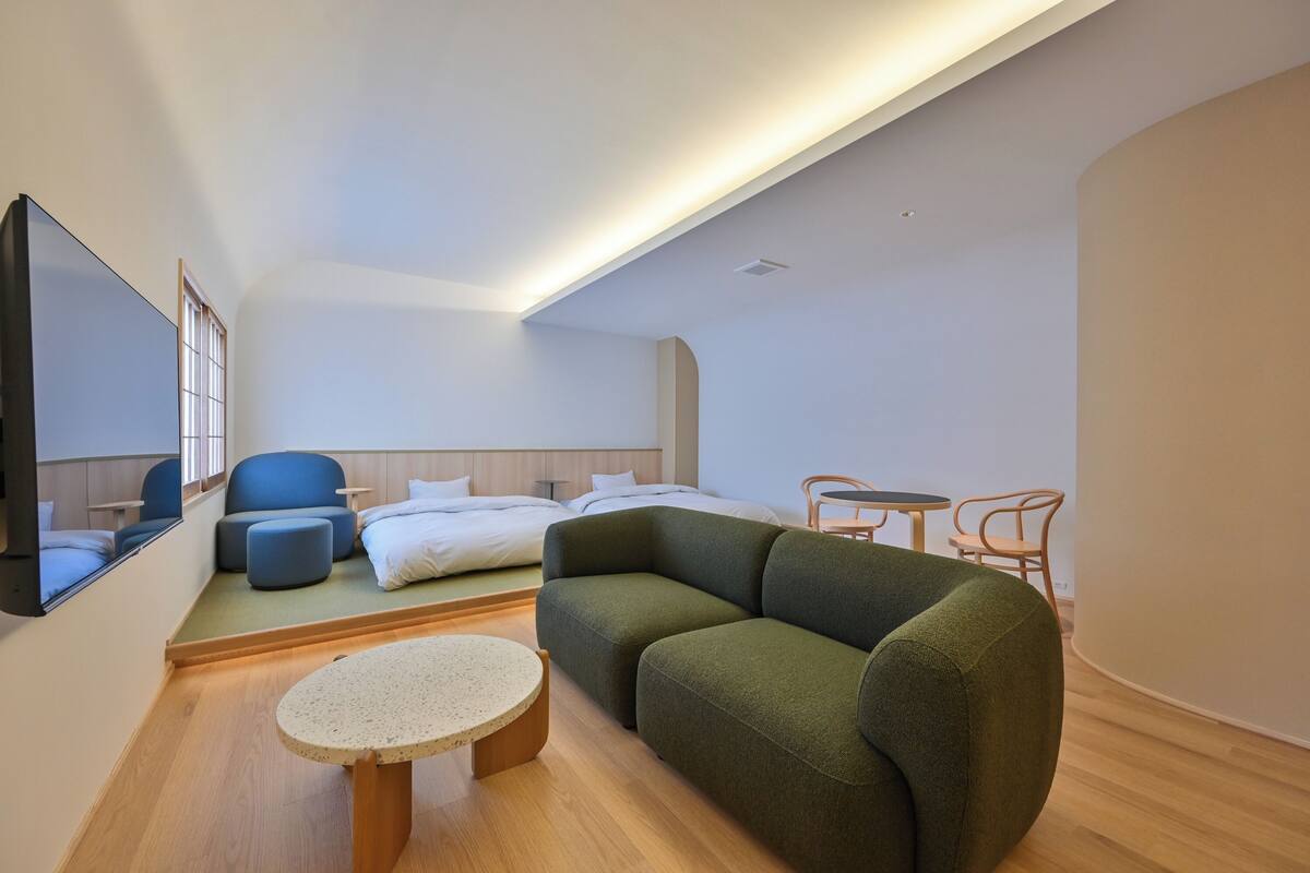 Una habitación de hotel moderna con sofá, una mesa redonda, cama, televisor y un pequeño comedor.
