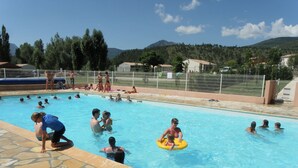 Une piscine avec des personnes dans l’eau, une terrasse dallée de pierres et une clôture entourant l’espace piscine.