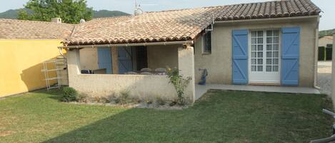 A small house with a tiled roof, a blue door, and a small garden area.