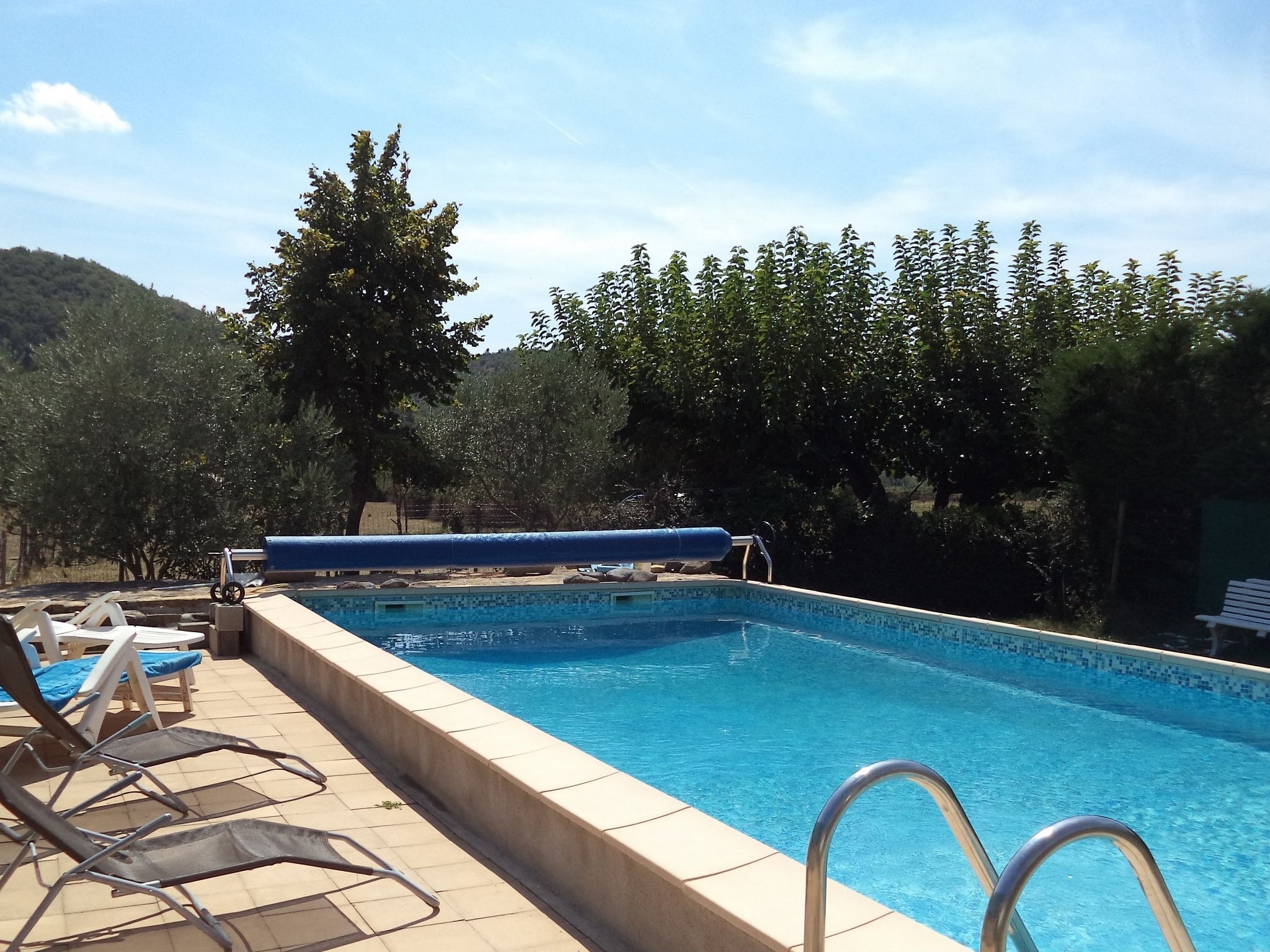 Una piscina con sillones de descanso y un toldo azul.