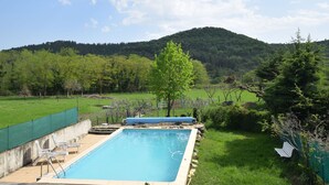 Una piscina rectangular con un cielo azul despejado y una colina boscosa al fondo.