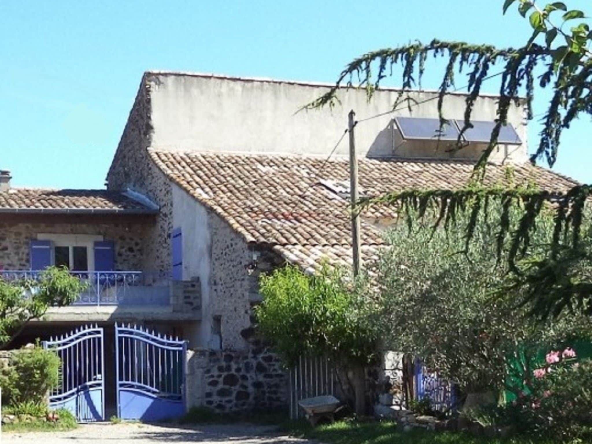A stone building with a tiled roof, a gated entrance, and a small garden area.