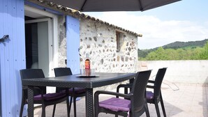 Un área de comedor al aire libre con un muro de piedra, una puerta azul y vistas a las colinas.
